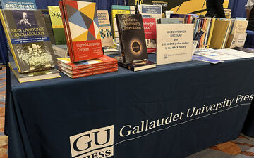 A rectangular table with a navy blue tablecloth that reads Gallaudet University Press. On top of the table are several books, faced out. 